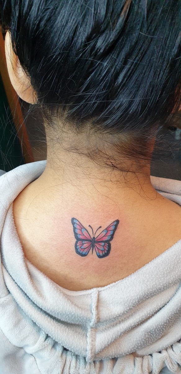 Small colour butterfly tattoo on the back of the neck at Divine Arts Tattoos.
