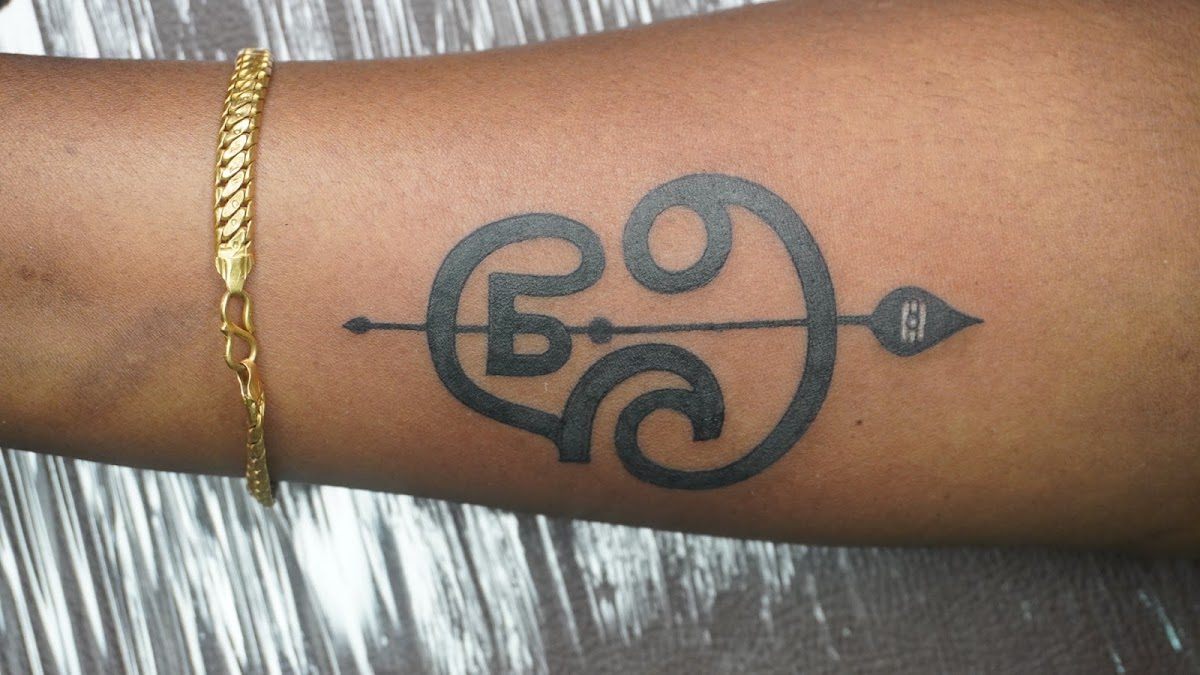 Fine-line Malayalam script and arrow tattoo on a forearm at Divine Arts Tattoos.