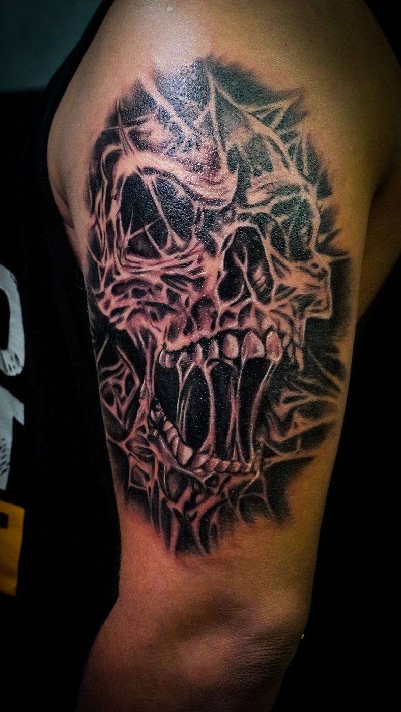 Detailed black-and-grey skull tattoo on an upper arm at Divine Arts Tattoos, Walthamstow.