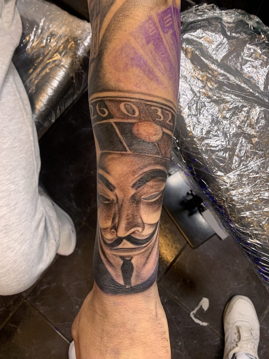 Black-and-grey portrait tattoo of a masked figure on a forearm at Divine Arts Tattoos.